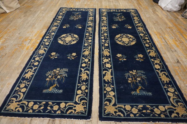 Pair of dark blue runners with beige floral borders and medallions displayed on distressed light wood floors.