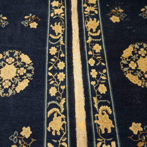 High-pile navy blue rug with tan and light blue floral designs and vertical striped borders on wood flooring.