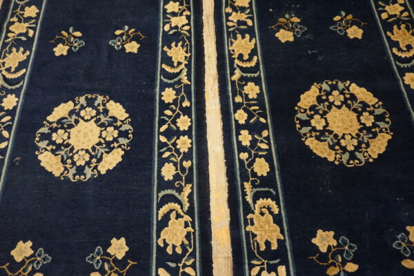 High-pile navy blue rug with tan and light blue floral designs and vertical striped borders on wood flooring.