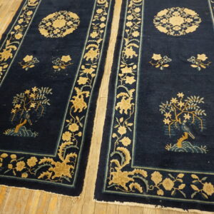 Two navy rugs with golden yellow botanical scenes and borders lie on wide wood planks.