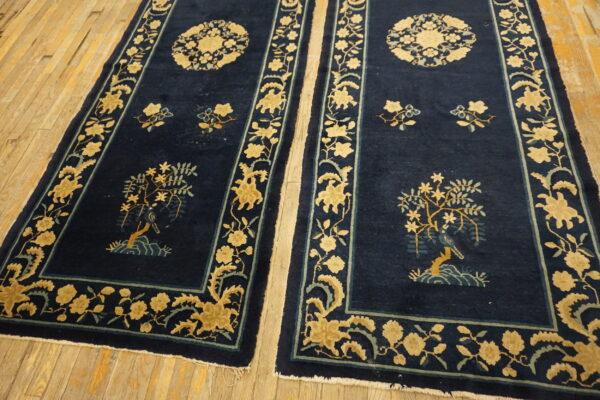 Two navy rugs with golden yellow botanical scenes and borders lie on wide wood planks.