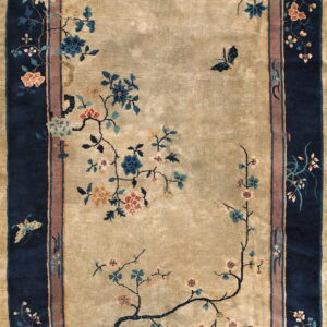 A beige rug with a wide navy blue border features delicate flowering vines and butterflies.
