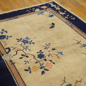 Cream area rug featuring detailed blue and coral floral vines and a wide navy border on wood flooring.