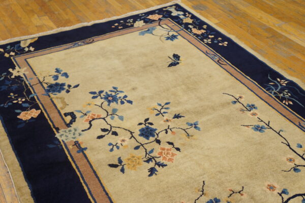 Cream area rug featuring detailed blue and coral floral vines and a wide navy border on wood flooring.