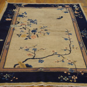 Low pile beige and navy rug with multicolor floral motifs and butterflies on polished wood planks.