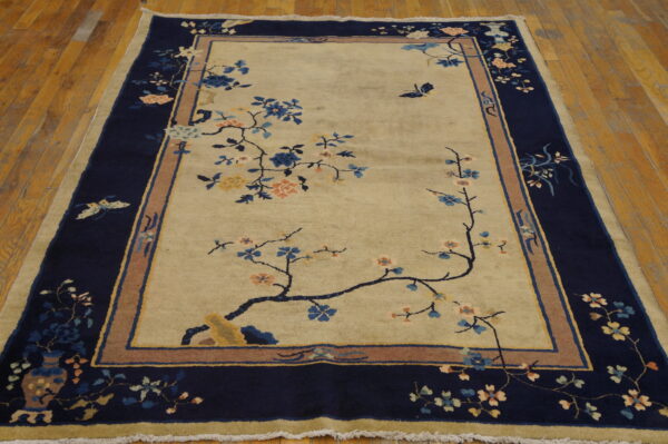Low pile beige and navy rug with multicolor floral motifs and butterflies on polished wood planks.