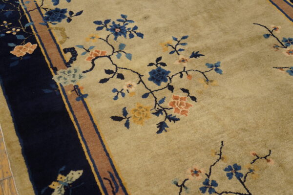 Close up of a tan rug with blue, peach, and yellow floral patterns and a dark blue border.