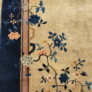Beige rug featuring sprawling blue and coral flowers adjacent to a navy and rust striped border.