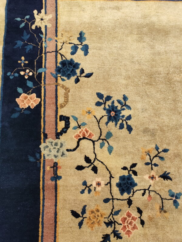 Beige rug featuring sprawling blue and coral flowers adjacent to a navy and rust striped border.