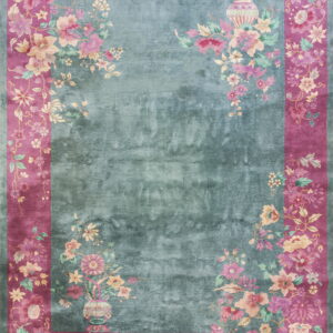 Low-pile rug with a mottled teal center and wide magenta border adorned with detailed pink flowers.