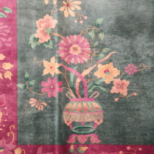 Close-up of a rug showing a teal field with a floral vase motif and a magenta border.