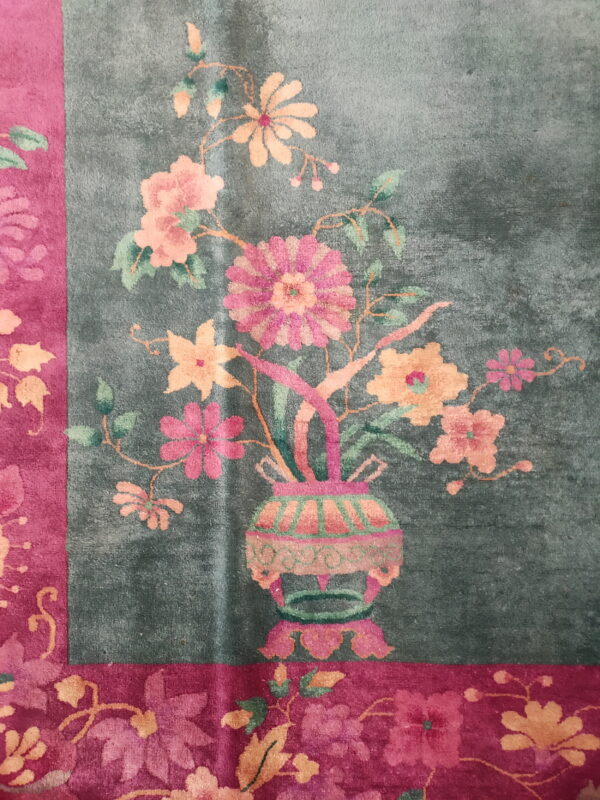 Close-up of a rug showing a teal field with a floral vase motif and a magenta border.