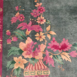 Plush teal rug with a magenta border featuring a vase filled with bright pink and peach flowers.