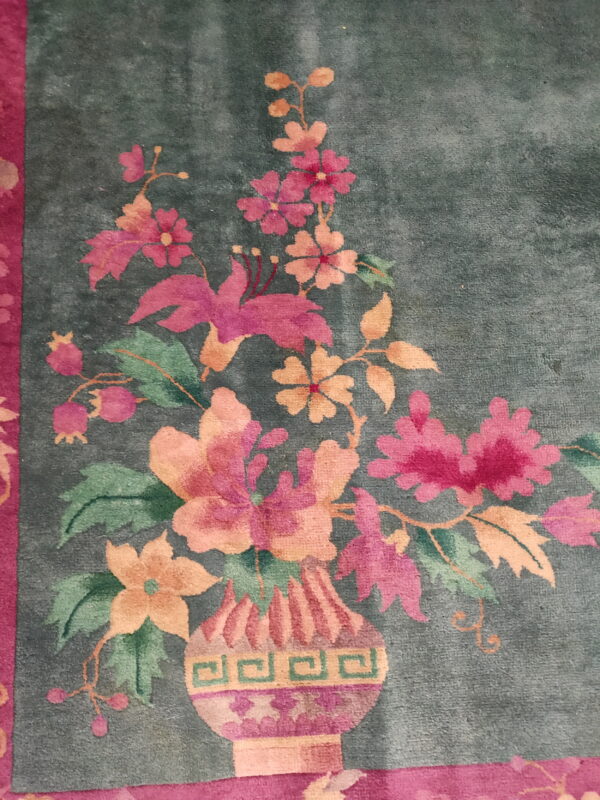 Plush teal rug with a magenta border featuring a vase filled with bright pink and peach flowers.