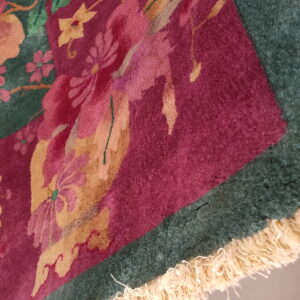Close-up of a high-pile rug with magenta floral patterns on a dark green and burgundy background, showing fringe.