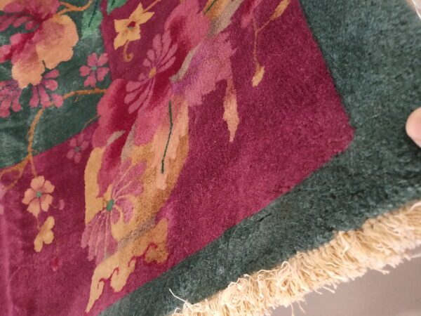 Close-up of a high-pile rug with magenta floral patterns on a dark green and burgundy background, showing fringe.