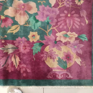 Magenta and teal rug with colorful floral motifs rests on white tile near a white shoe.