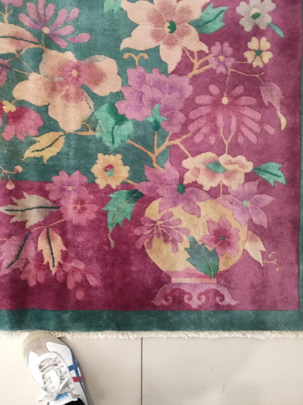 Magenta and teal rug with colorful floral motifs rests on white tile near a white shoe.
