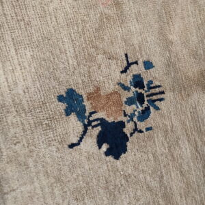 Beige low-pile rug close-up featuring a stylized flower motif in navy, teal, and tan colors.
