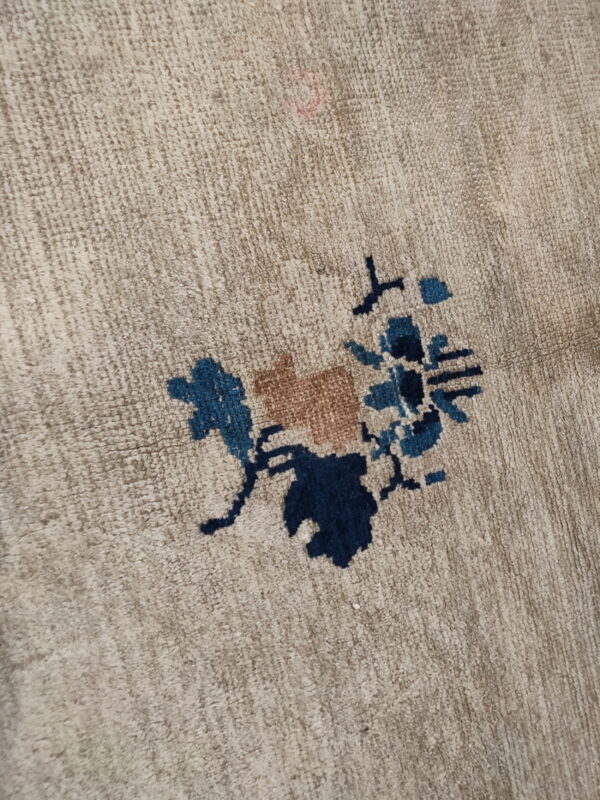 Beige low-pile rug close-up featuring a stylized flower motif in navy, teal, and tan colors.