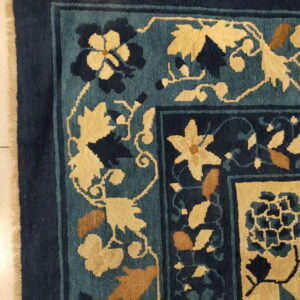Blue, teal, and cream floral rug detail, showing the border design resting on light-colored tiles.