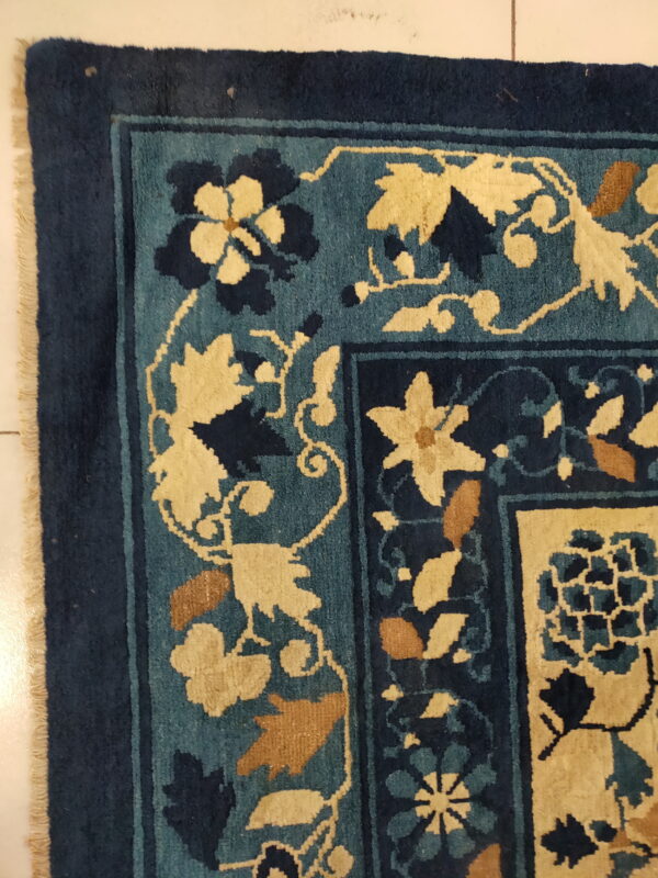 Blue, teal, and cream floral rug detail, showing the border design resting on light-colored tiles.