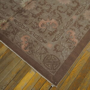 Brown ornamental rug with peach accents and geometric borders covers distressed wood flooring.