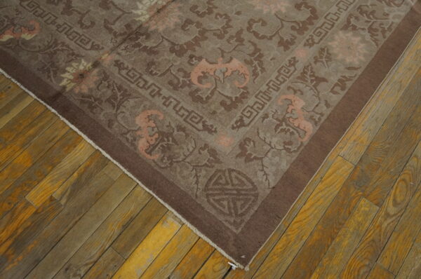 Brown ornamental rug with peach accents and geometric borders covers distressed wood flooring.
