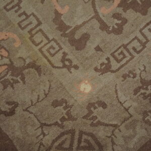 Close-up of a brownish-gray low-pile rug patterned with dark brown geometric and salmon-pink curvilinear designs.