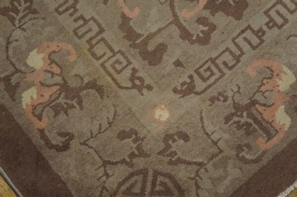 Close-up of a brownish-gray low-pile rug patterned with dark brown geometric and salmon-pink curvilinear designs.