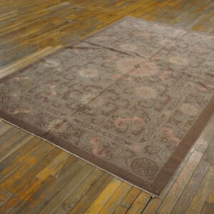 Low pile rug in muted taupe and pink floral patterns rests on distressed wooden floorboards.