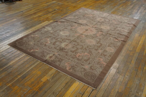 Low pile rug in muted taupe and pink floral patterns rests on distressed wooden floorboards.
