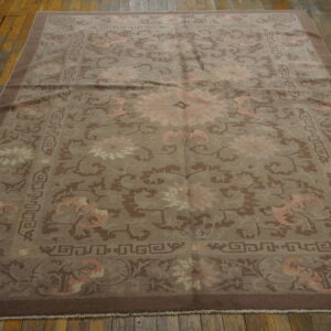Muted brown and pale pink patterned rug with wide borders lies flat on rustic wood flooring.