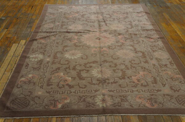 Muted brown and pale pink patterned rug with wide borders lies flat on rustic wood flooring.