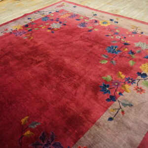 Crimson rug with a floral border featuring colorful blue, yellow, and purple blooms on wood flooring.