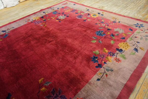 Crimson rug with a floral border featuring colorful blue, yellow, and purple blooms on wood flooring.