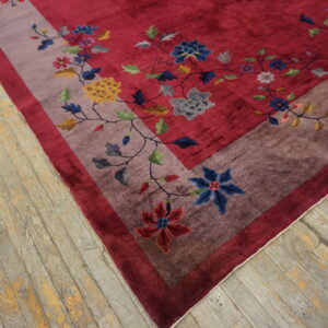A deep red floral rug featuring a wide mauve border rests on weathered gray wood flooring.