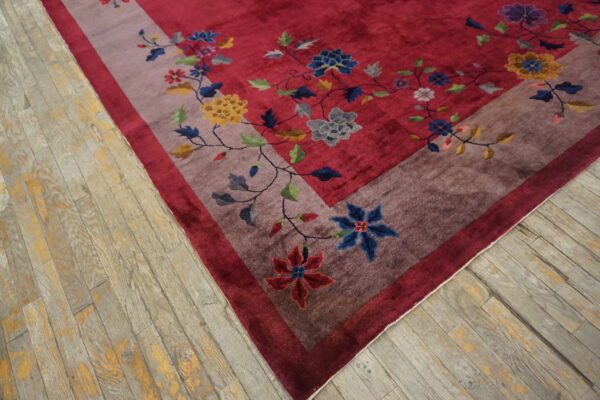 A deep red floral rug featuring a wide mauve border rests on weathered gray wood flooring.