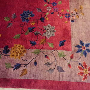 Deep pink rug with a floral vine pattern and a wide mauve border lying on wood flooring.