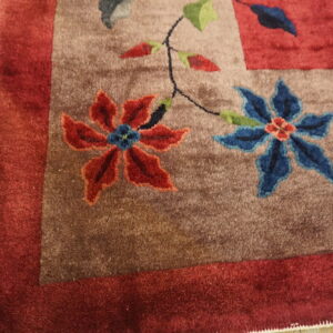 High-pile floral rug with red and blue flowers on a brown field next to light wood flooring.