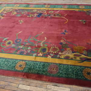 Deep red rug with lush, colorful floral patterns and wide gold and green geometric borders on wood floor.