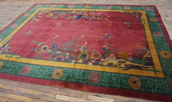 Deep red rug with lush, colorful floral patterns and wide gold and green geometric borders on wood floor.