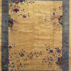 A lustrous golden tan rug features a wide dark blue border with elaborate multi-colored floral and vine motifs.