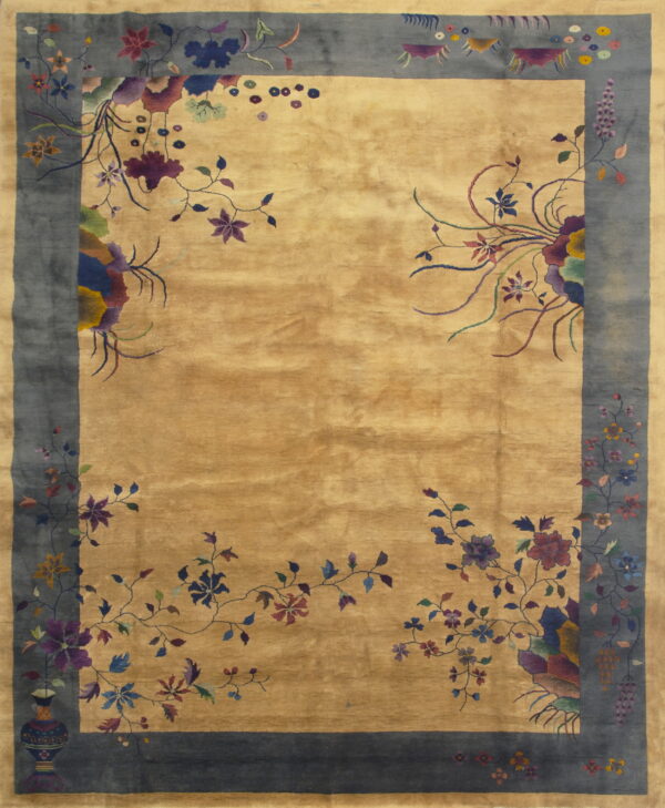 A lustrous golden tan rug features a wide dark blue border with elaborate multi-colored floral and vine motifs.