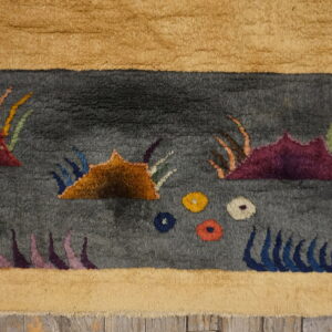 Textured gray rug with stylized maroon and orange shapes, bordered in tan, resting on wood planks.