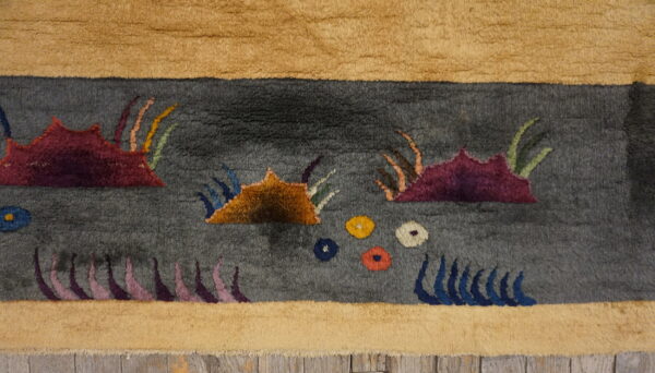 Textured gray rug with stylized maroon and orange shapes, bordered in tan, resting on wood planks.