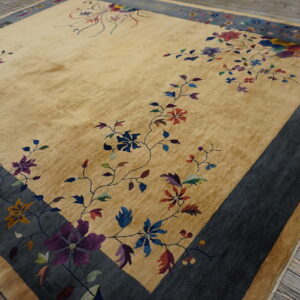 Gold-tan rug featuring multicolored flowers and a broad dark gray border sits on wooden floorboards.