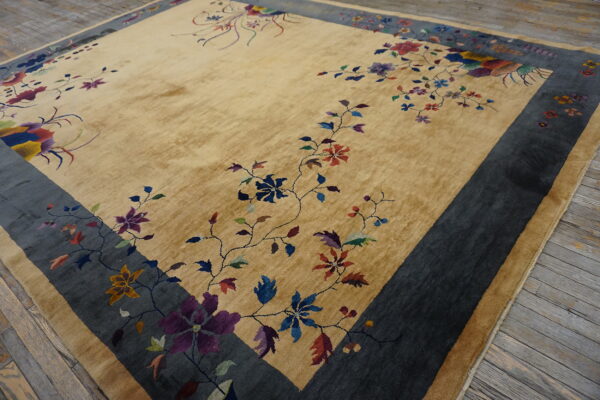 Gold-tan rug featuring multicolored flowers and a broad dark gray border sits on wooden floorboards.