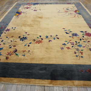 Gold rug with colorful floral vines and a wide slate blue border, lying on distressed wooden planks.