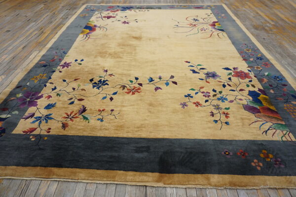 Gold rug with colorful floral vines and a wide slate blue border, lying on distressed wooden planks.